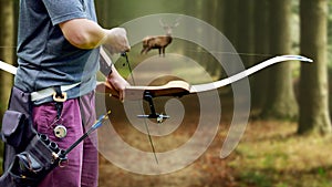 A bow hunter aiming at a White tail buck against