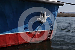 The bow of a moored ship, a red and blue ship with a white anchor
