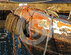 The bow of an old rusty iron canal boat moored with ropes on a jetty with reflections in dark water