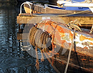 Bow of an old rusty iron canal boat moored with ropes on a jetty with reflections in dark water