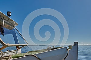 Bow of a steel excursion ship with white paint in front of a calm lake with blue sky and lots of copy space