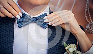 Bow tie on the groom`s suit. Bride`s hands touch the tie of her betrothed, close up. Theme of the wedding, newlyweds, love