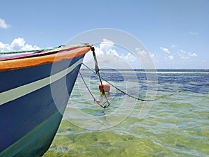 Bow of a typical Caribbean fishing boat chained to a red round buoy in turquoise waters of a lagoon in the Caribbean Sea. Tropical