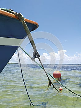 Bow of a typical Caribbean fishing boat chained to a red round buoy in turquoise waters of a lagoon in the Caribbean Sea. Tropical