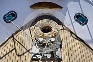 Bow of white yacht. Bay with thick rope lies on wooden deck. Rope is wound on anchor post. Top view. Close-up.