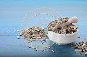 Bowl with aromatic dried lemongrass and scoop on light blue wooden table. Space for text