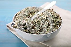 Bowl with aromatic dried lemongrass and spoon on light blue wooden table, closeup