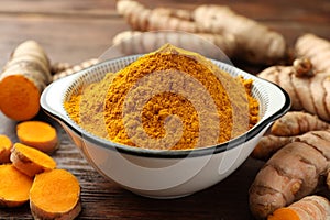 Bowl with aromatic turmeric powder and cut roots on wooden table, closeup