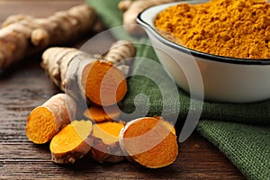 Bowl with aromatic turmeric powder and cut roots on wooden table, closeup