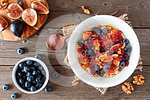 Bowl of autumn oatmeal with figs, blueberries, pomegranates and sweet jelly, top view table scene over wood