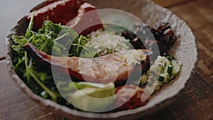 Bowl with baked fish, fresh avocado, arugula and vegetables in cafe