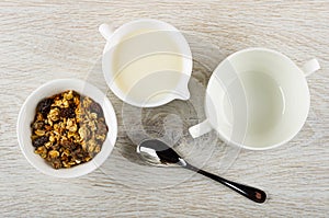 Bowl with baked muesli, pitcher with yogurt, empty bowl, spoon on wooden table. Top view