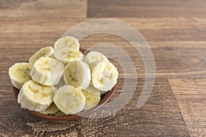 Bowl with banana slices on wooden background