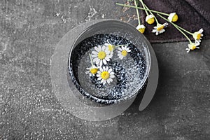 Bowl with beautiful camomile flowers and water on grey table