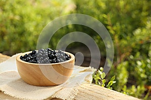 Bowl of bilberries on wooden table outdoors, space for text