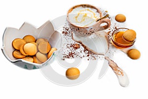 Bowl with biscuit, cup of coffee cocoa with overflowing foam on dirty white background sprinkled with cocoa powder, glass bowl