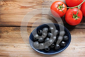 Bowl of black olives and fresh tomatoes on the vine on rustic wooden table background. Pasta or salad ingredients.