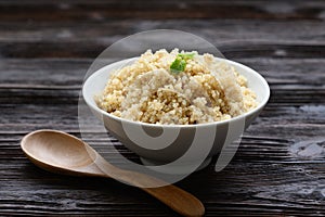 Bowl of boiled quinoa on wood background