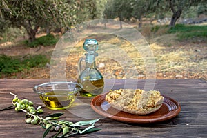Bowl and bottle with extra virgin olive oil, olives, a fresh branch of olive tree and cretan rusk dakos on wooden table.