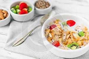 Bowl of breakfast cereals with milk, strawberry, kiwi, almonds, and seeds.