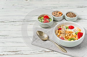 Bowl of breakfast cereals with milk, strawberry, kiwi, almonds, and seeds.