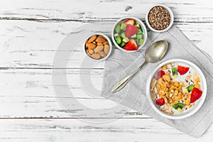 Bowl of breakfast cereals with milk, strawberry, kiwi, almonds, and seeds.