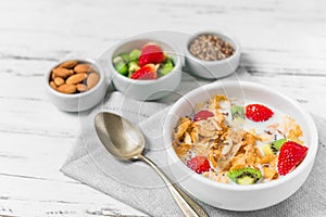 Bowl of breakfast cereals with milk, strawberry, kiwi, almonds, and seeds.