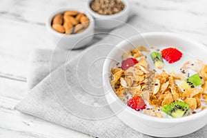 Bowl of breakfast cereals with milk, strawberry, kiwi, almonds, and seeds.