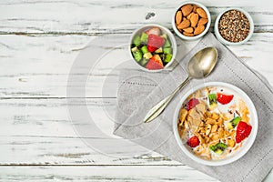 Bowl of breakfast cereals with milk, strawberry, kiwi, almonds, and seeds.