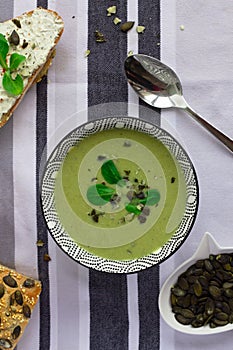 Bowl of broccoli cream soup, grain bread with pumpkin seeds and spoon on the table, healthy vegetarian eating concept. Balanced di