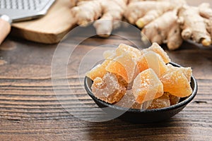 Bowl of candied ginger pieces and ginger roots on wooden kitchen table