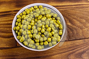 Bowl with canned green peas  on wooden table. Top view