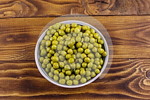 Bowl with canned green peas on wooden table. Top view