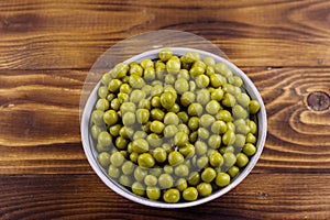 Bowl with canned green peas on wooden table. Top view