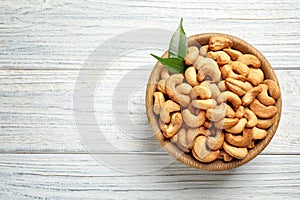 Bowl with cashew nuts on wooden table, top view.