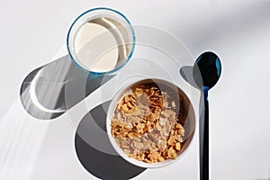 Bowl of cereal and glass of milk on white background. Healthy breakfast with cornflakes and milk. Top view, copy space. Hard light