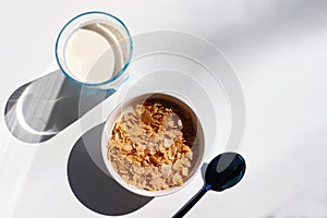 Bowl of cereal and glass of milk on white background. Healthy breakfast with cornflakes and milk. Top view, copy space. Hard light