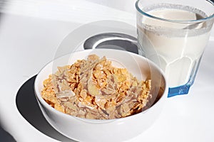 Bowl of cereal and glass of milk on white background. Healthy breakfast with cornflakes and milk. Top view, copy space. Hard light