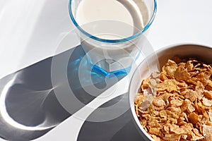 Bowl of cereal and glass of milk on white background. Healthy breakfast with cornflakes and milk. Top view, copy space. Hard light