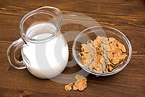 Bowl with cereal and milk jug on wood