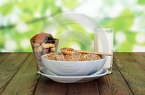 Bowl cereals, nuts, dried fruit, glass milk on abstract green.