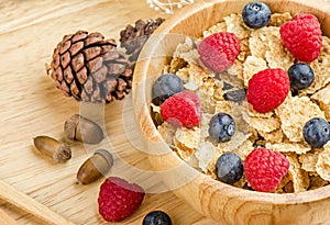 Bowl of cereals with raspberries and blueberrys on a wooden table.