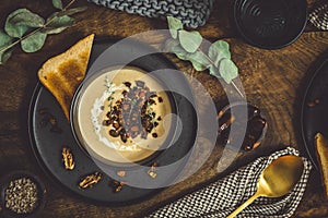 Bowl of chestnut soup with rosted topping, cream and bread in a black bowl on rustic wooden background