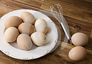 Bowl of chicken eggs, whisk, wooden background.