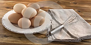 Bowl of chicken eggs, whisk, wooden background.