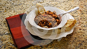 Bowl of chili with beans in a white bowl with bread on the side.