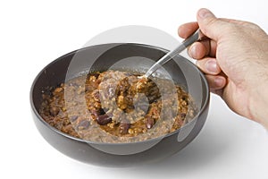 Bowl of chilli and hand holding spoon