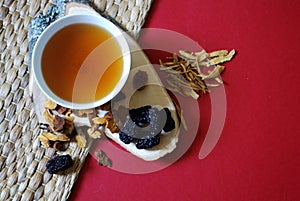 Bowl of chinese herb tea with pieces of astragalus and huang qi roots and jujubes on red background. Top view.