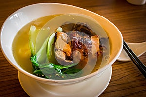 A bowl of chinese wanton noodle soup with chicken char siew and vegeatable on top