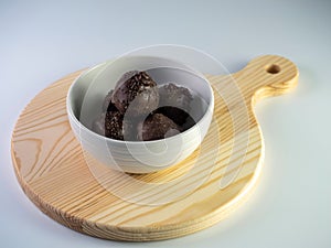 A bowl with chocolate balls placed on wooden chopping board isolated on a white background